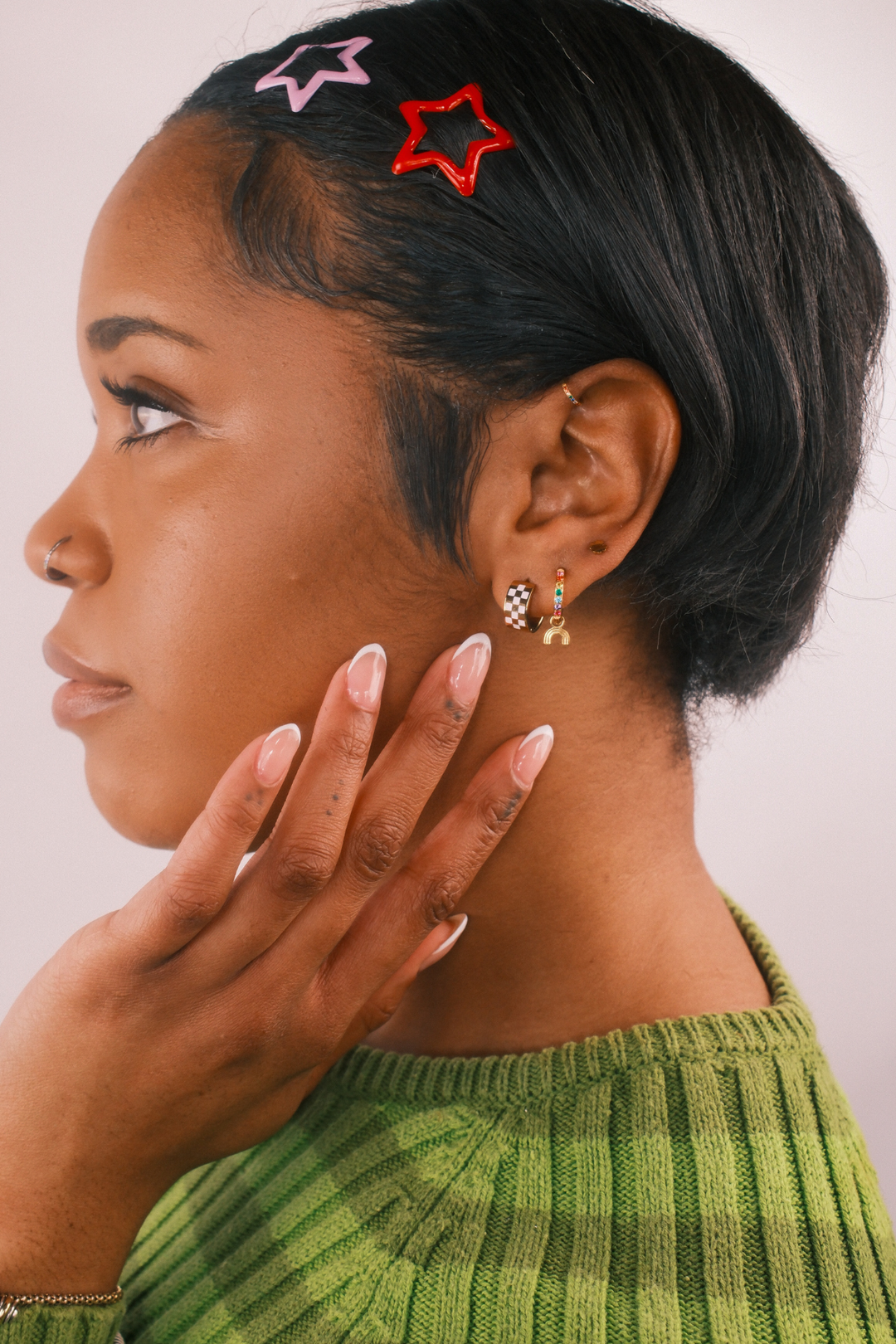 Close up of a model wearing multiple earrings against a blank background