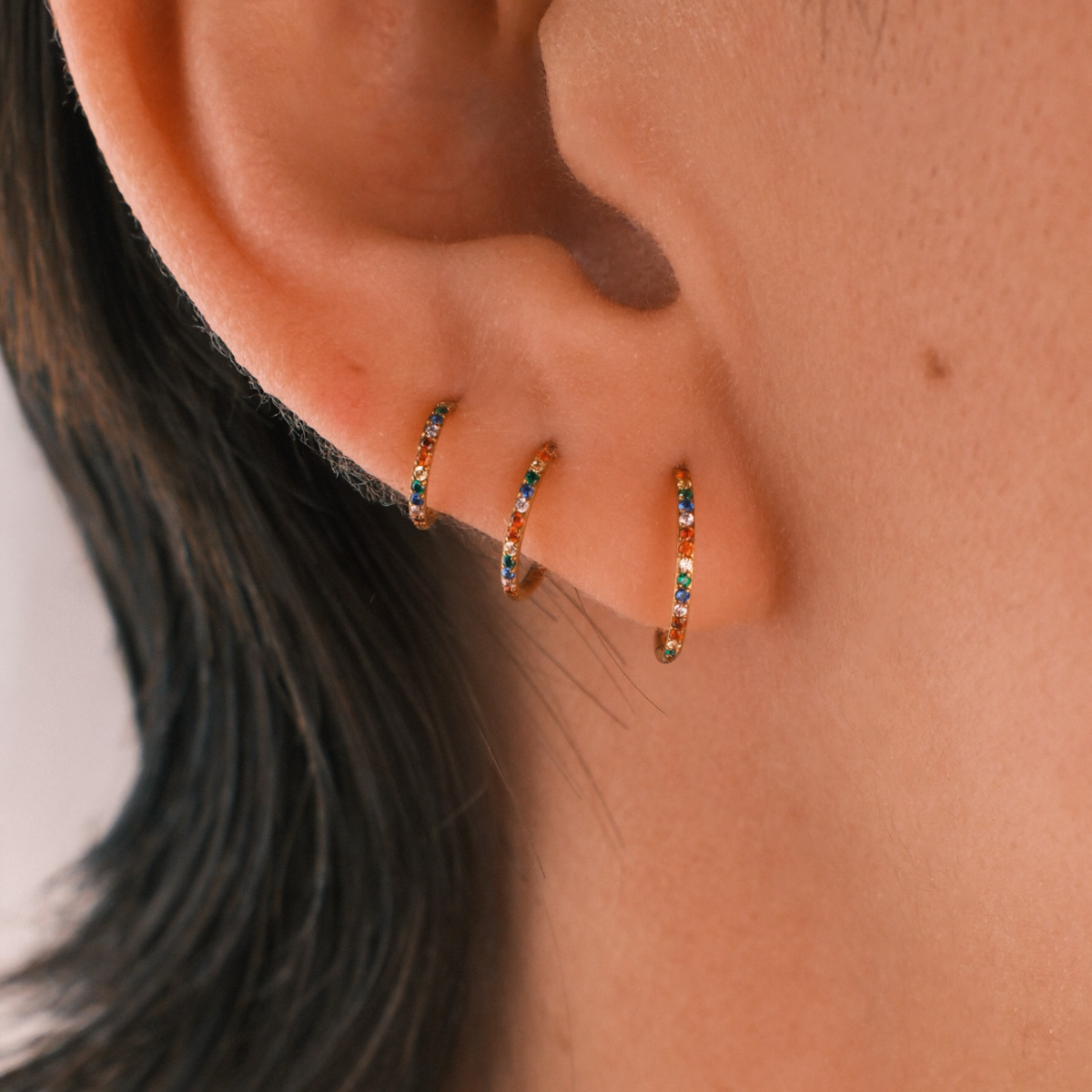 Close-up of an ear wearing three gold hoop earrings with small gemstones.
