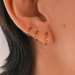 Close-up of an ear wearing three gold hoop earrings with small gemstones.