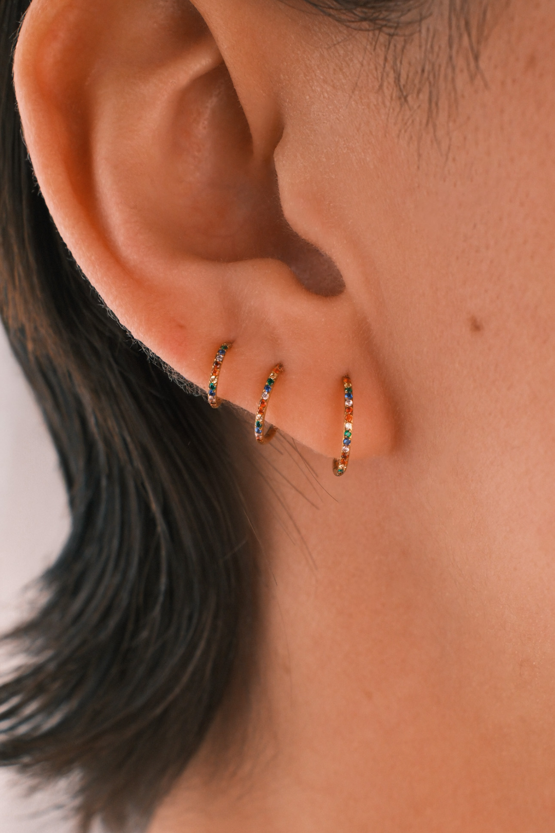 Close-up of an ear wearing three gold hoop earrings with small gemstones.