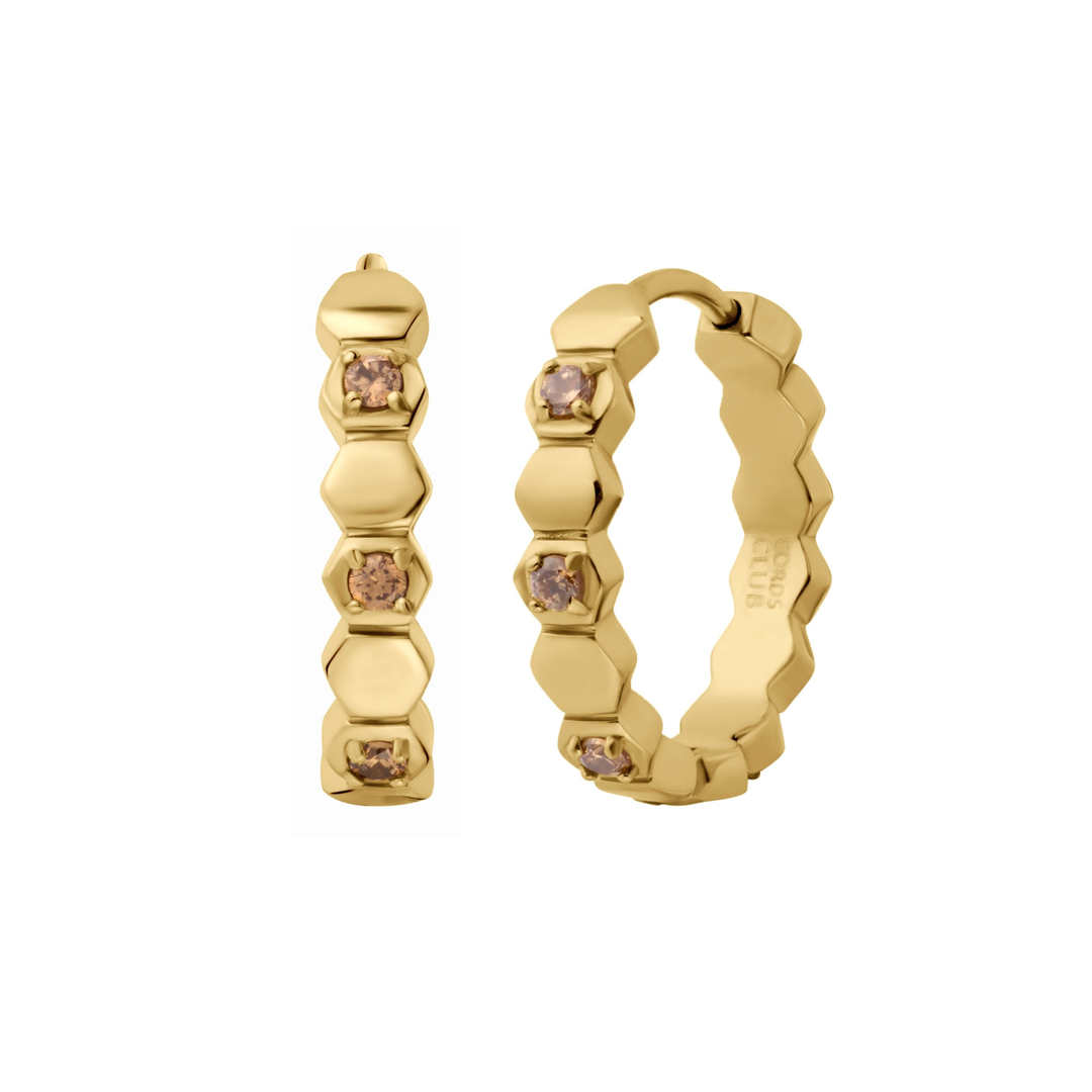 Close up of a hoop earring made from stacked hexagon shapes with a honey colored zirconia stone set into every other hexagon shape. Hoop made from 18k gold-plated316L Surgical Steel with a honey-colored zirconia stone, against a white background. 