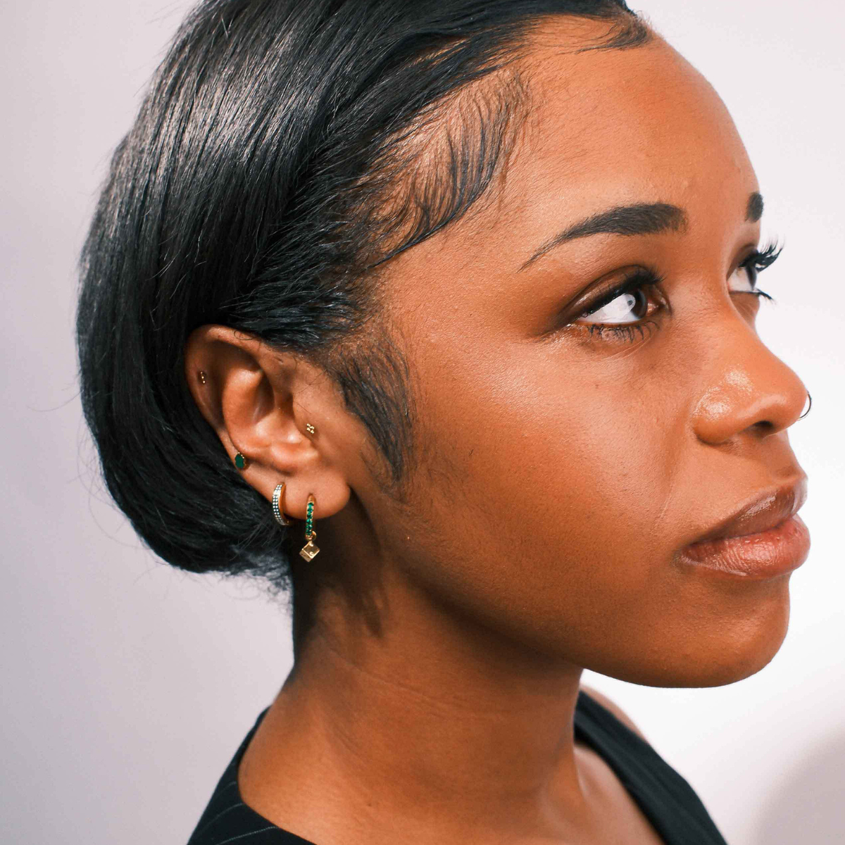 Close-up of an ear with multiple earrings on a neutral background