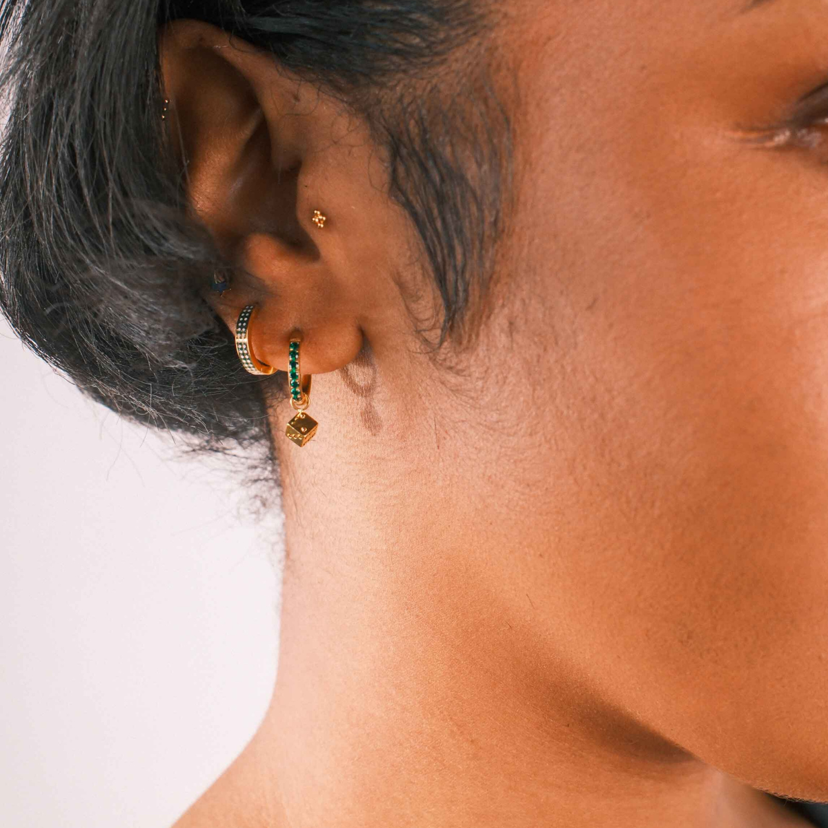 Close-up of an ear with multiple earrings on a neutral background