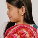 A  model wearing a hoop earring made from 18k gold-plated titanium metal, with geometric colored patterns that are reminiscent of quilt blocks in pinks, purple, blue, and green on a white background.
