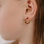 A close up of a model wearing a hoop earring with a softly scalloped edge resembling a daisy, made from 18k gold-plated titanium metal