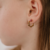 A close up of a model wearing a hoop earring with a softly scalloped edge resembling a daisy, made from 18k gold-plated titanium metal
