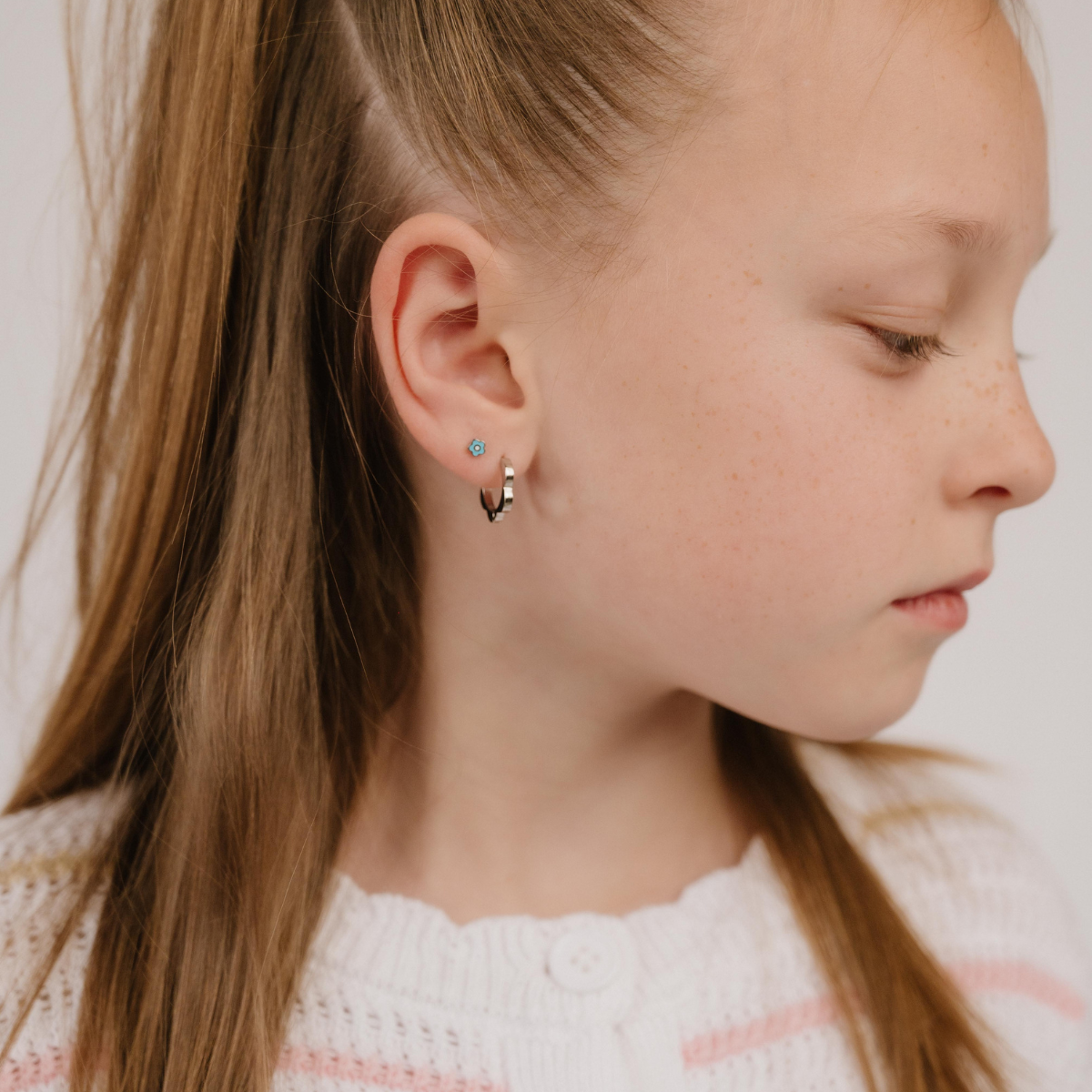 A close up of a model wearing a hoop earring with a softly scalloped edge resembling a daisy, made from titanium metal