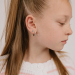 A close up of a model wearing a hoop earring with a softly scalloped edge resembling a daisy, made from titanium metal
