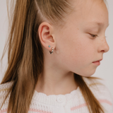 A close up of a model wearing a hoop earring with a softly scalloped edge resembling a daisy, made from titanium metal