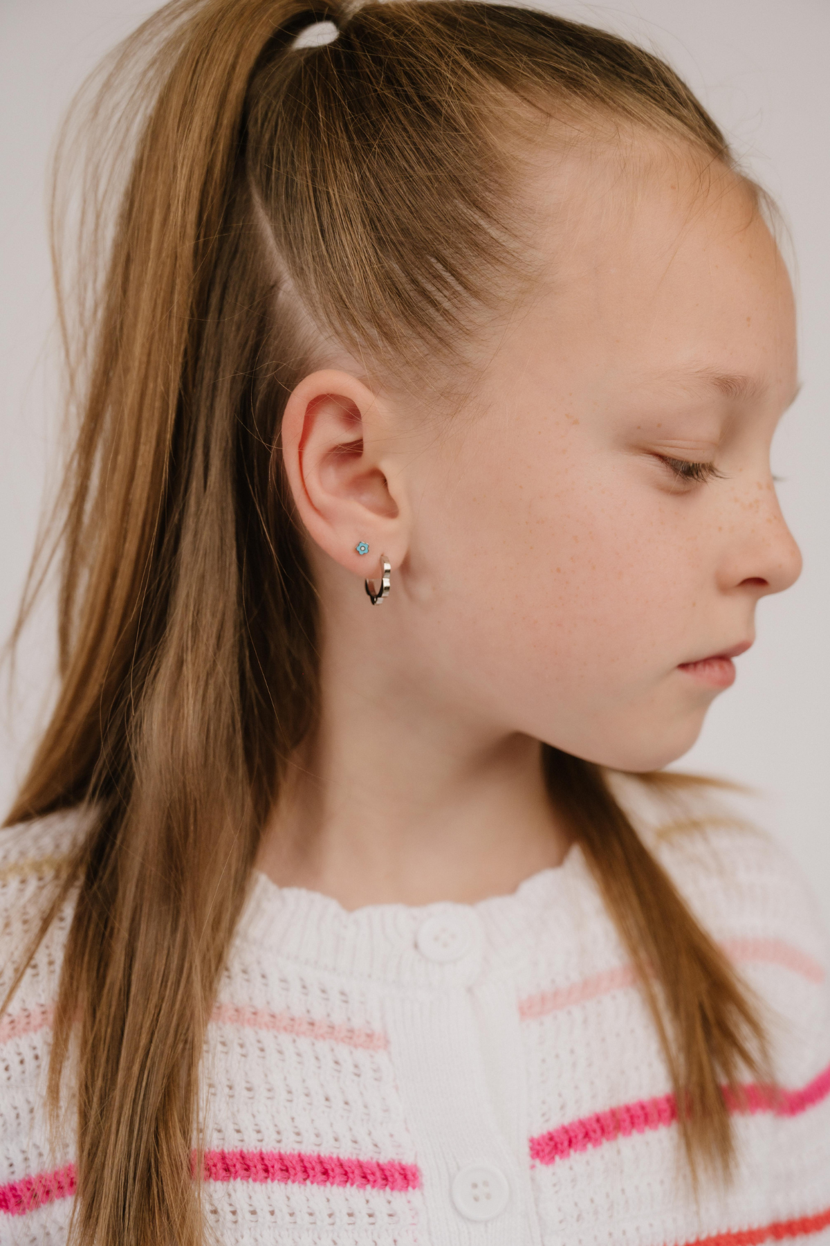 A close up of a model wearing a hoop earring with a softly scalloped edge resembling a daisy, made from titanium metal