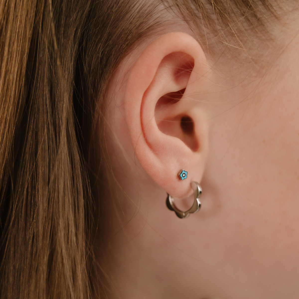 A close up of a model wearing a hoop earring with a softly scalloped edge resembling a daisy, made from titanium metal