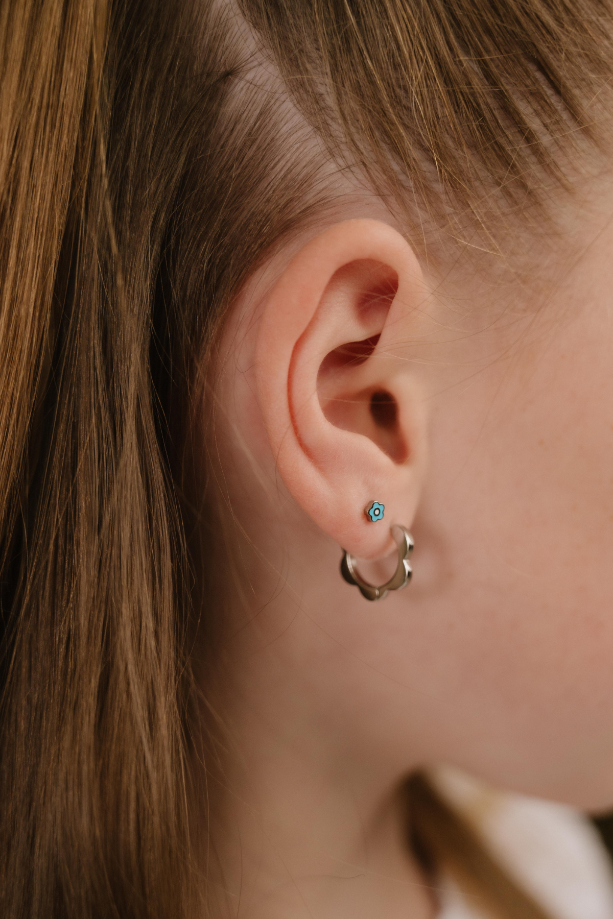 A close up of a model wearing a hoop earring with a softly scalloped edge resembling a daisy, made from titanium metal