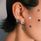 Close-up of a person wearing multiple earrings including a hoop with a channel of emerald green zirconia stones
