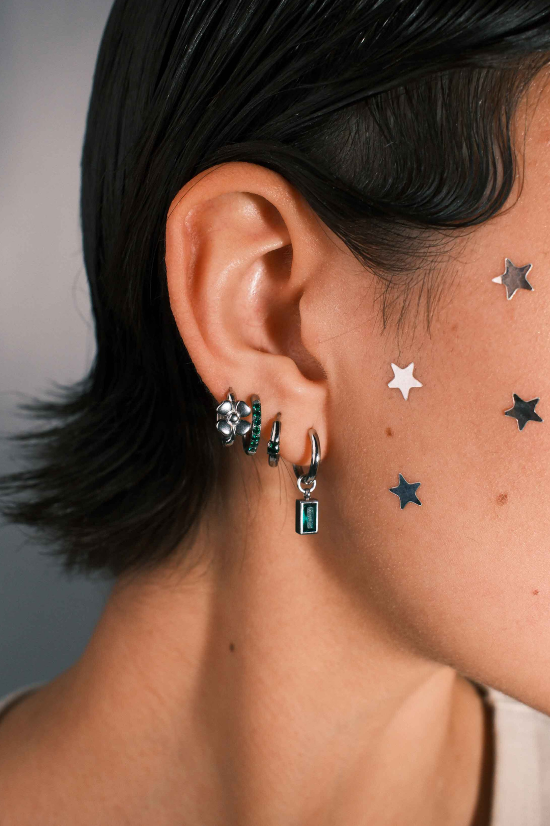 Close-up of a person wearing multiple earrings including a hoop with a channel of emerald green zirconia stones