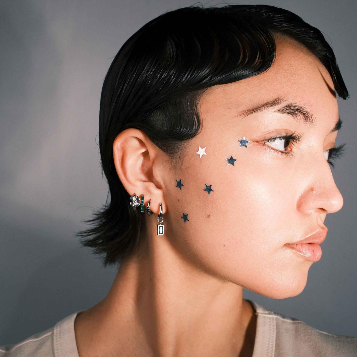Close-up of a person wearing multiple earrings including a hoop with a channel of emerald green zirconia stones