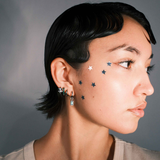 Close-up of a person wearing multiple earrings including a hoop with a channel of emerald green zirconia stones