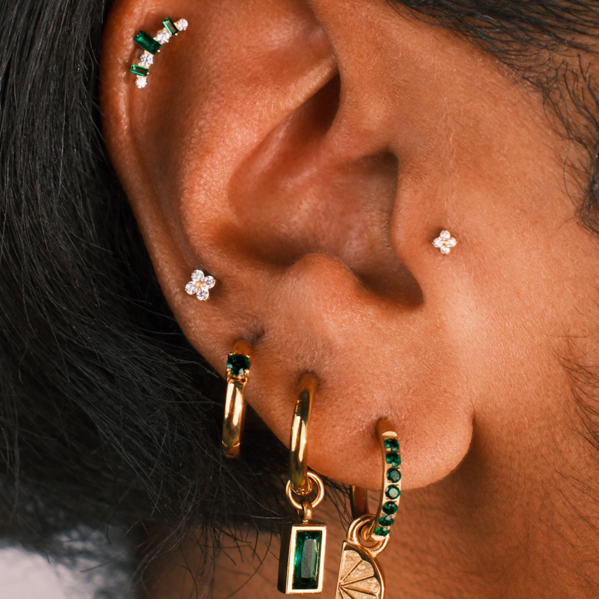 Close-up of an ear with multiple earrings including gold, green, and silver pieces.