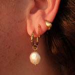 Close-up of an ear wearing gold hoop earrings with pearl drops.