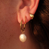 Close-up of an ear wearing gold hoop earrings with pearl drops.