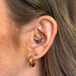 Close-up of an ear with gold hoop earrings and a small black and gold earring.