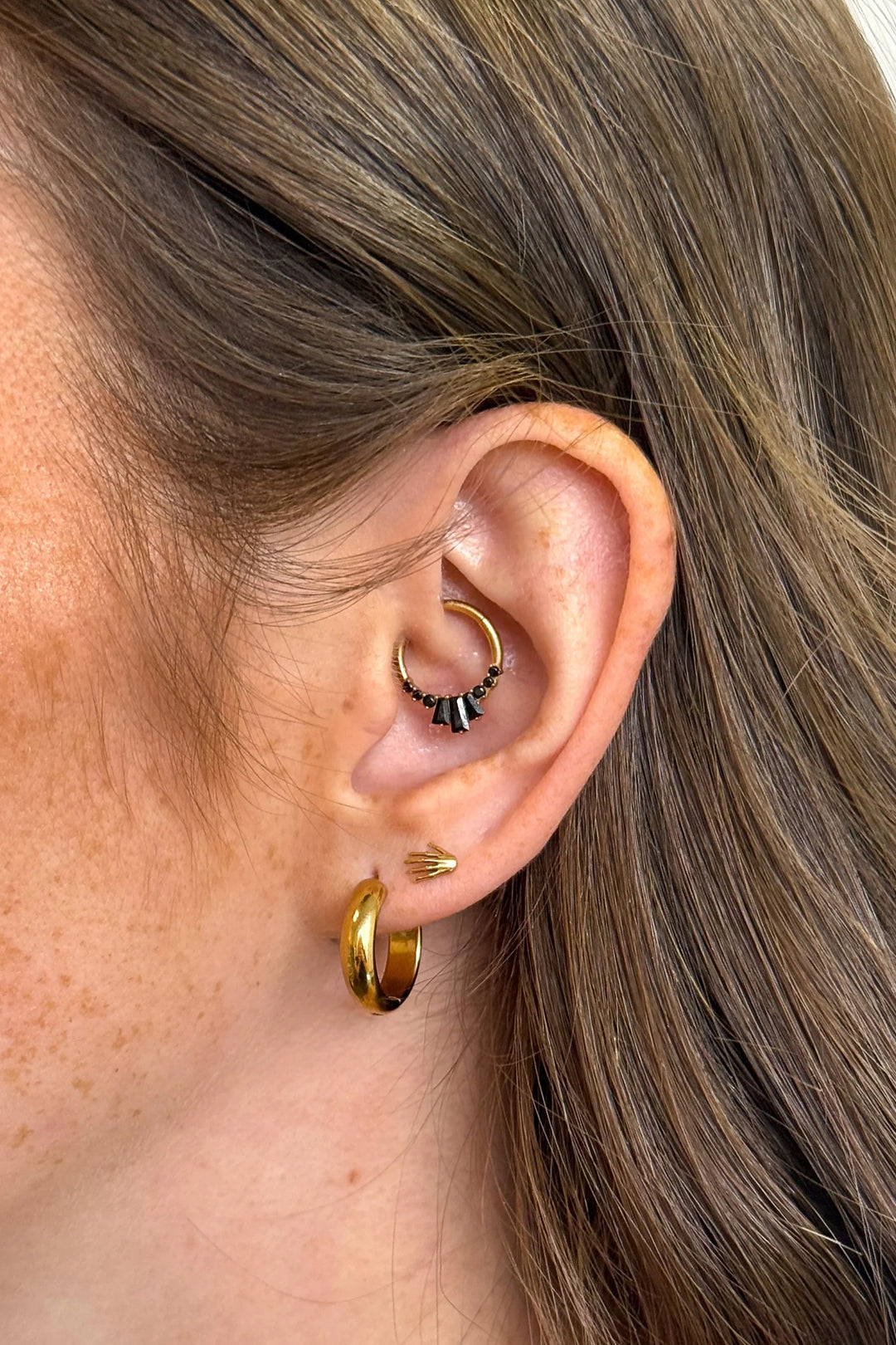 Close-up of an ear with gold hoop earrings and a small black and gold earring.