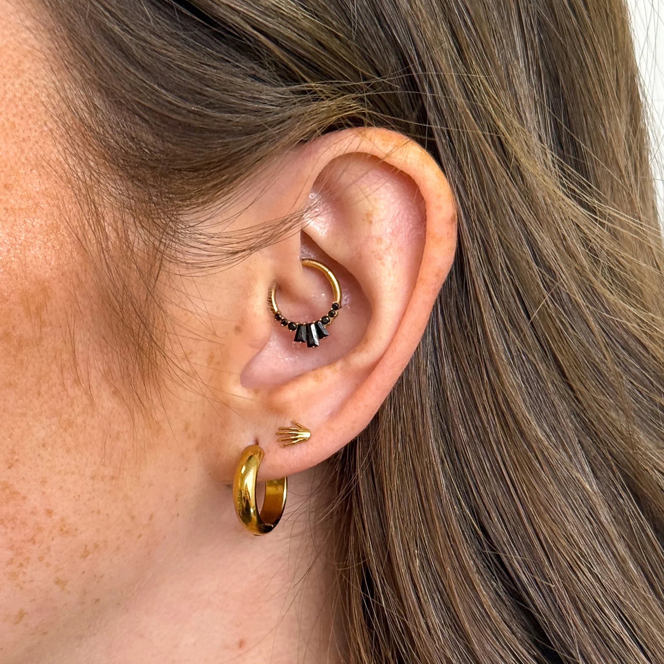 Close-up of an ear wearing gold hoops and stud earrings with a neutral background