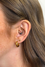 Close-up of an ear wearing gold hoops and stud earrings with a neutral background