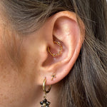 Close-up of an ear with gold hoop earrings and a black flower earring.