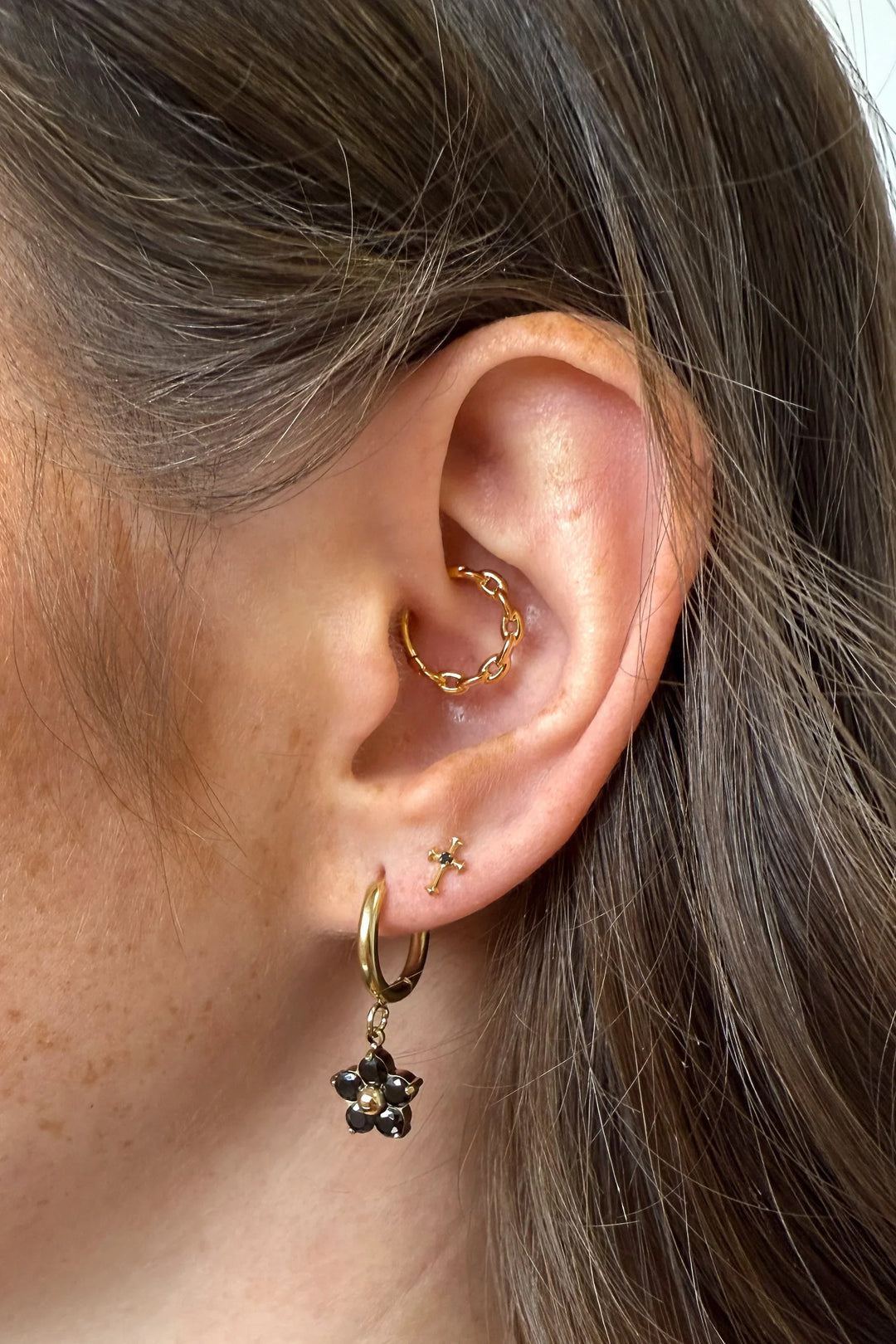 Close-up of an ear with gold hoop earrings and a black flower earring.