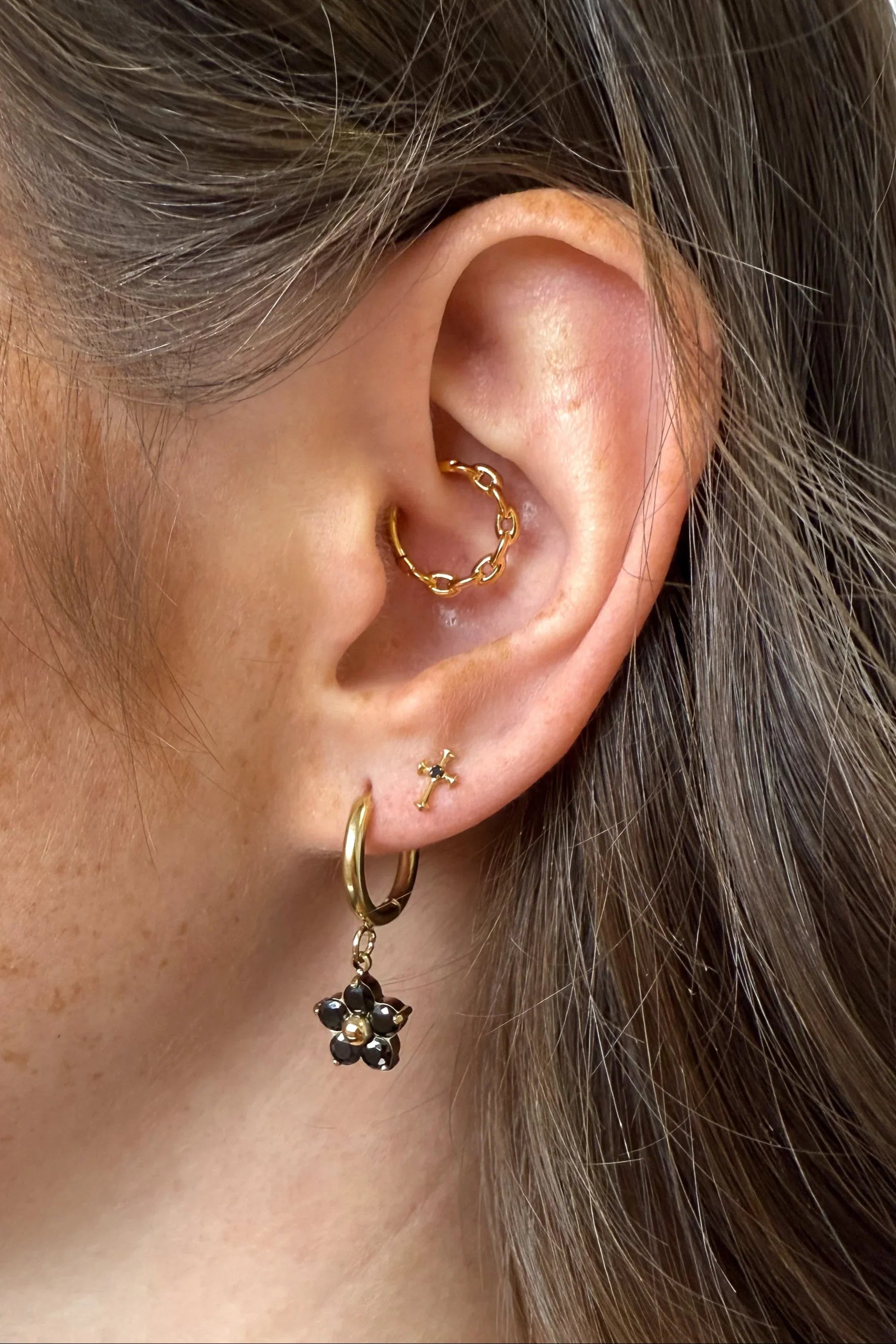 Close-up of an ear with gold hoop earrings and a black flower earring.