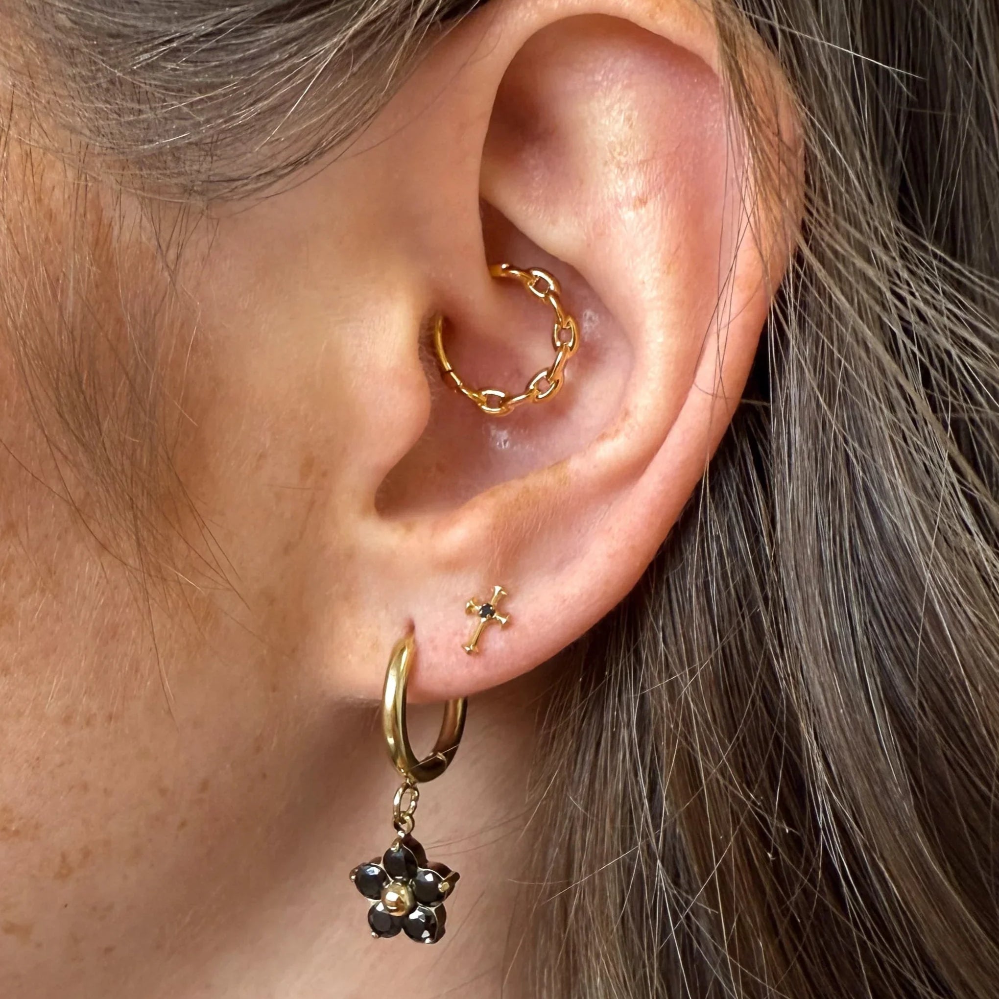 Close-up of an ear with gold hoop earrings and a black flower earring.