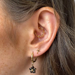 Close-up of an ear with gold hoop earrings and a black flower earring.