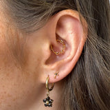 Close-up of an ear with gold hoop earrings and a black flower earring.