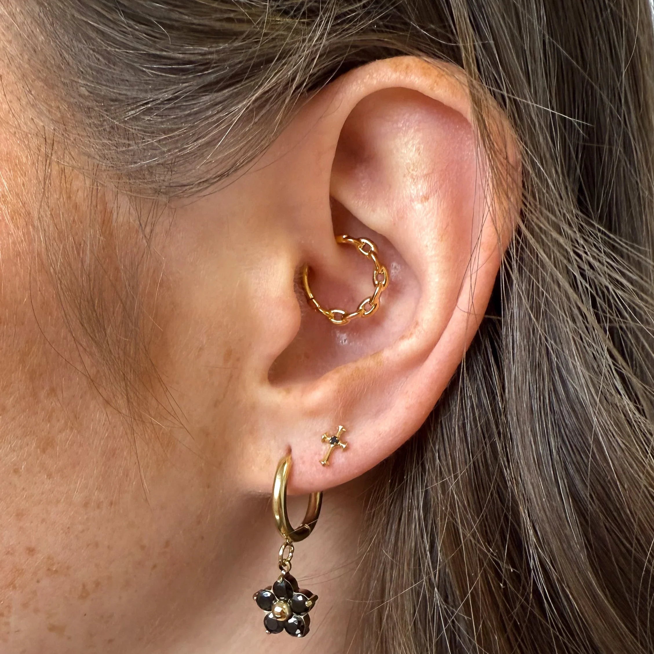 Close-up of an ear with gold hoop earrings and a black flower earring.