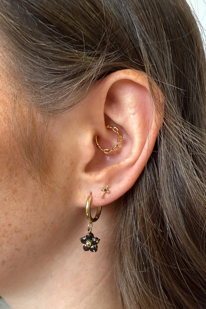 Close-up of an ear with gold hoop earrings and a black flower earring.