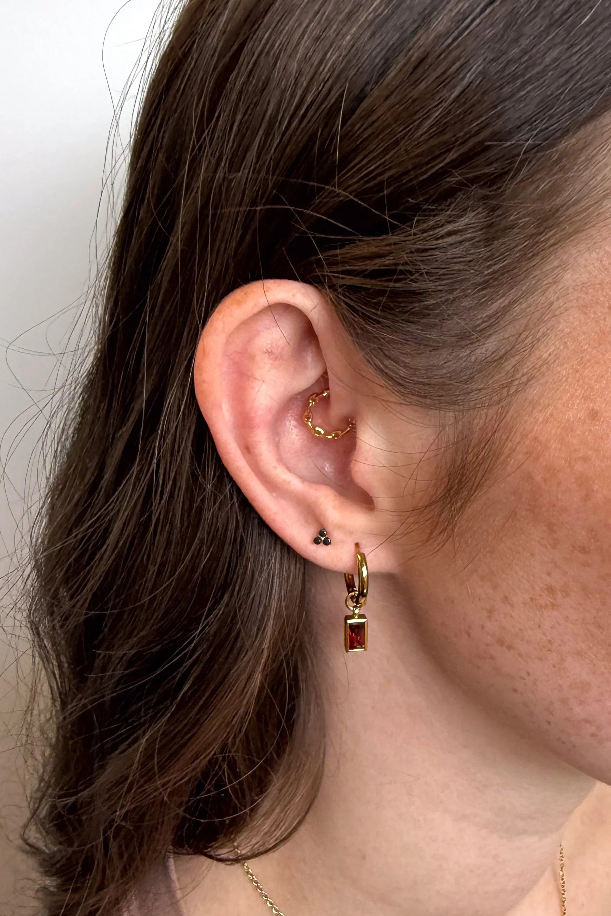 Close-up of an ear wearing gold hoop earrings with a plain background