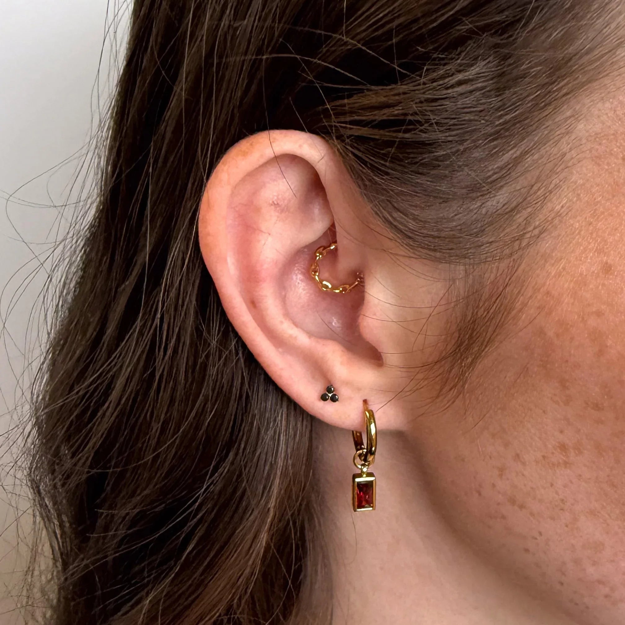 Close-up of an ear wearing gold hoop earrings with a plain background