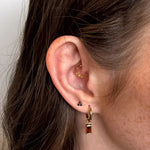 Close-up of an ear wearing gold hoop earrings with a plain background