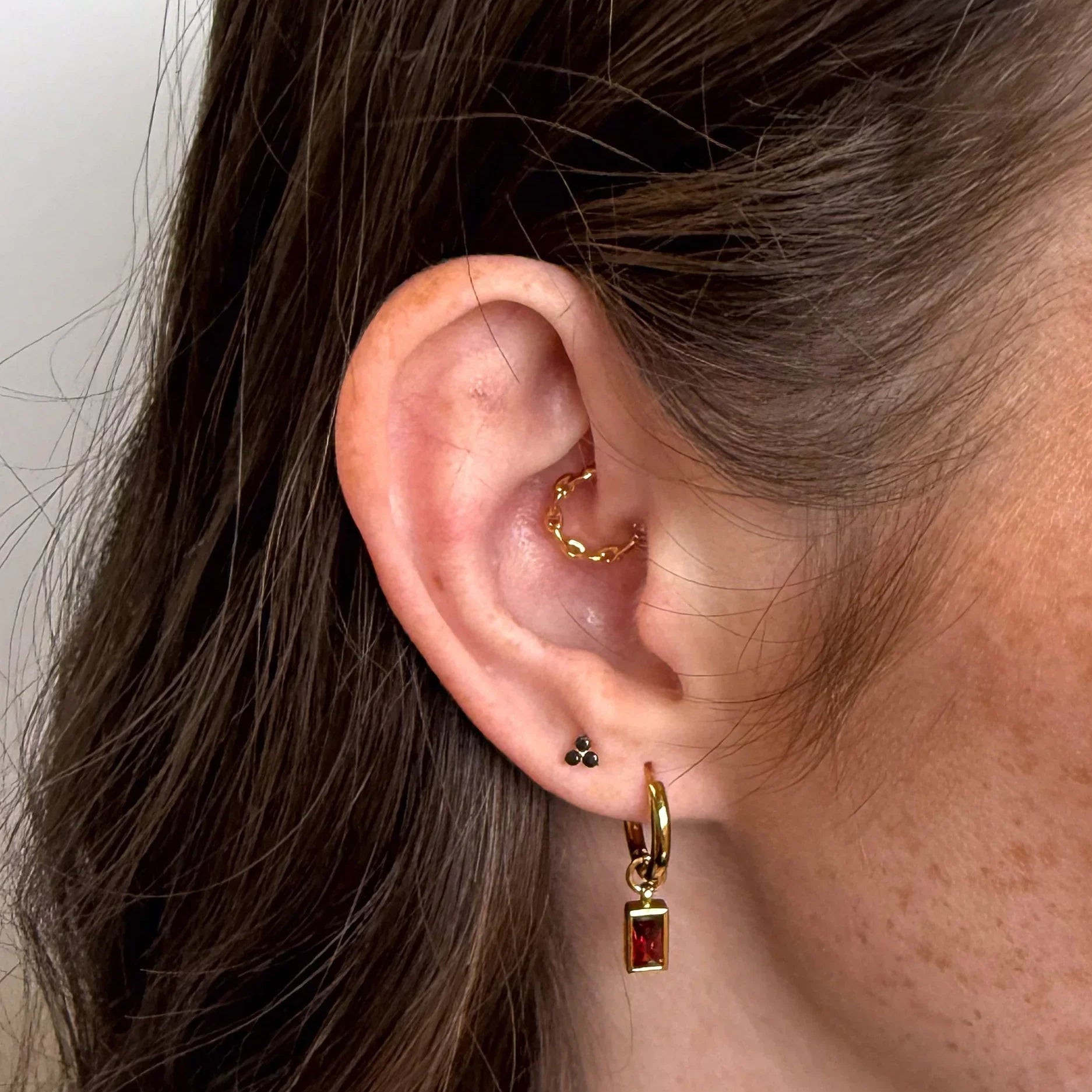 Close-up of an ear wearing gold hoop earrings with a plain background