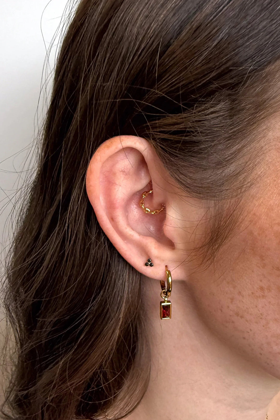 Close-up of an ear wearing gold hoop earrings with a plain background