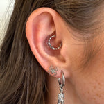 Close-up of an ear with silver hoop earrings featuring charms.