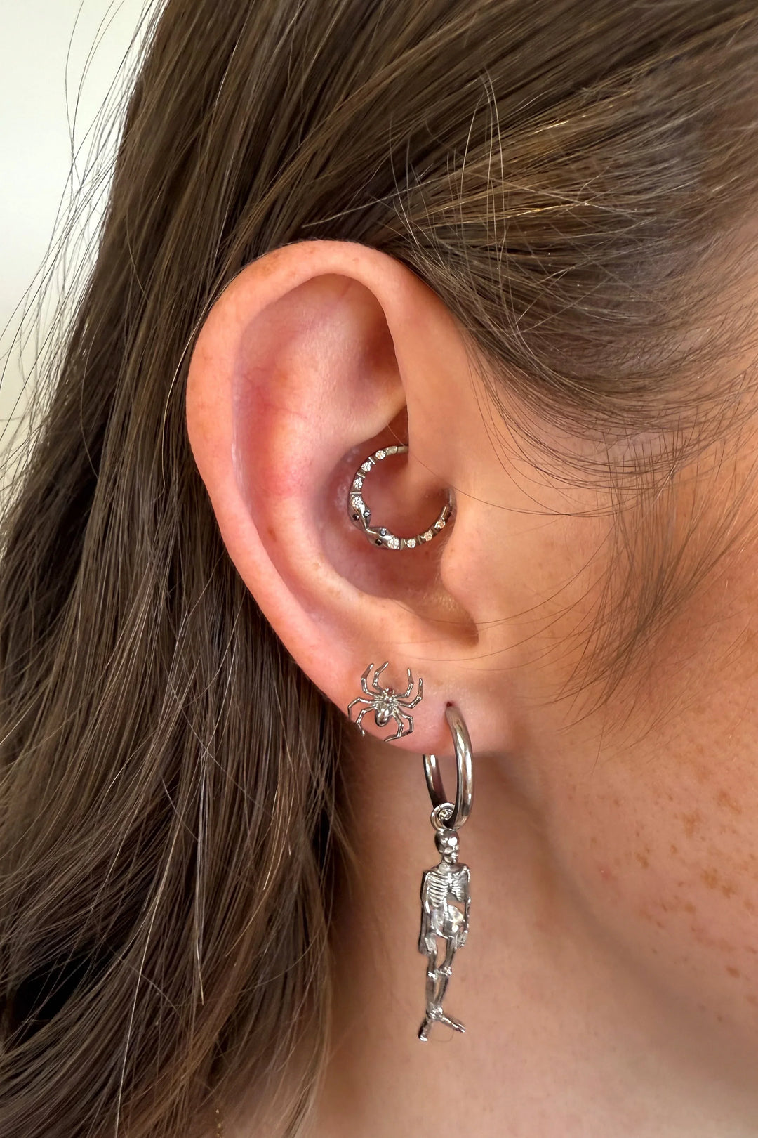 Close-up of an ear with silver hoop earrings featuring charms.