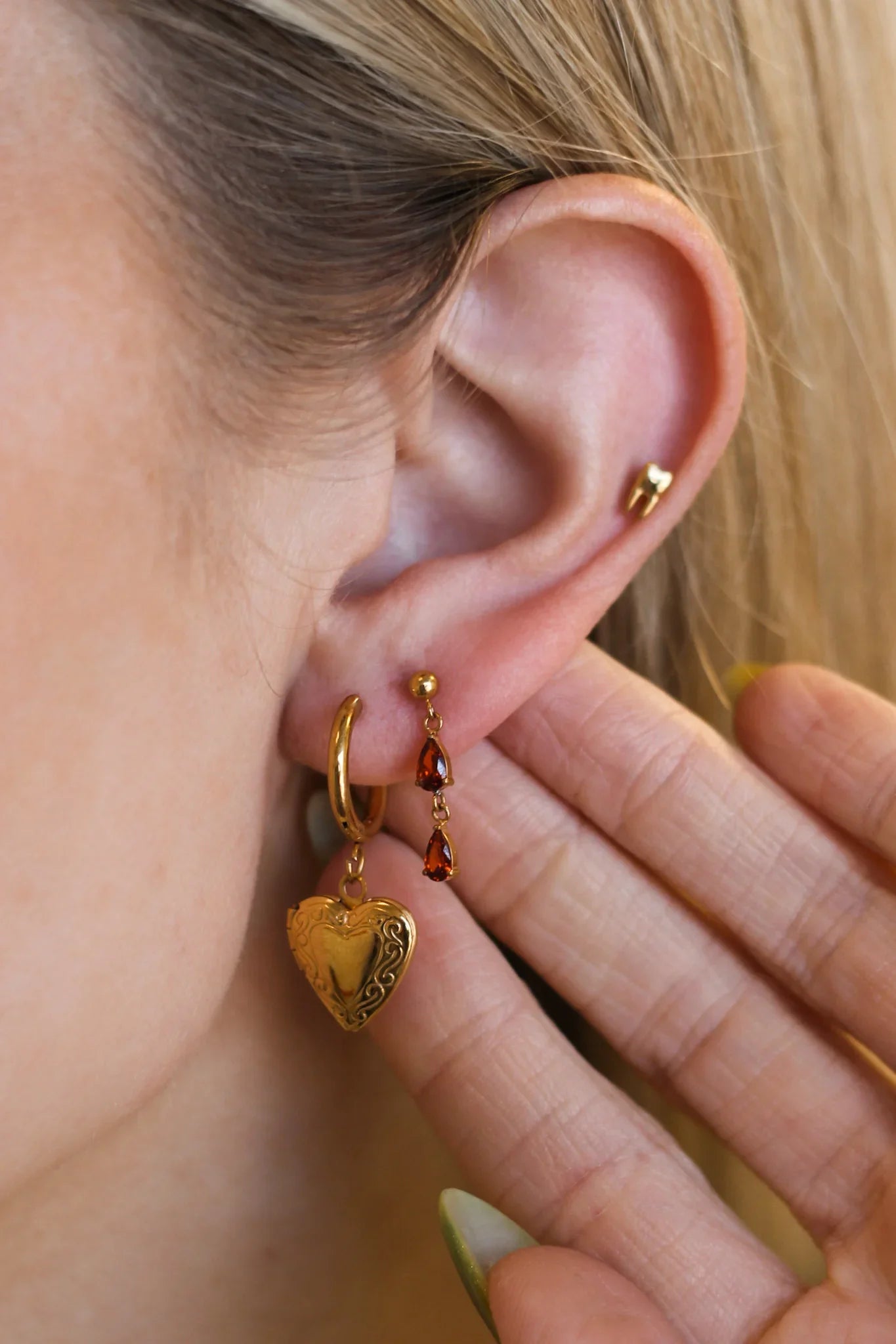 Close-up of a person wearing gold hoop earrings with heart-shaped charms.