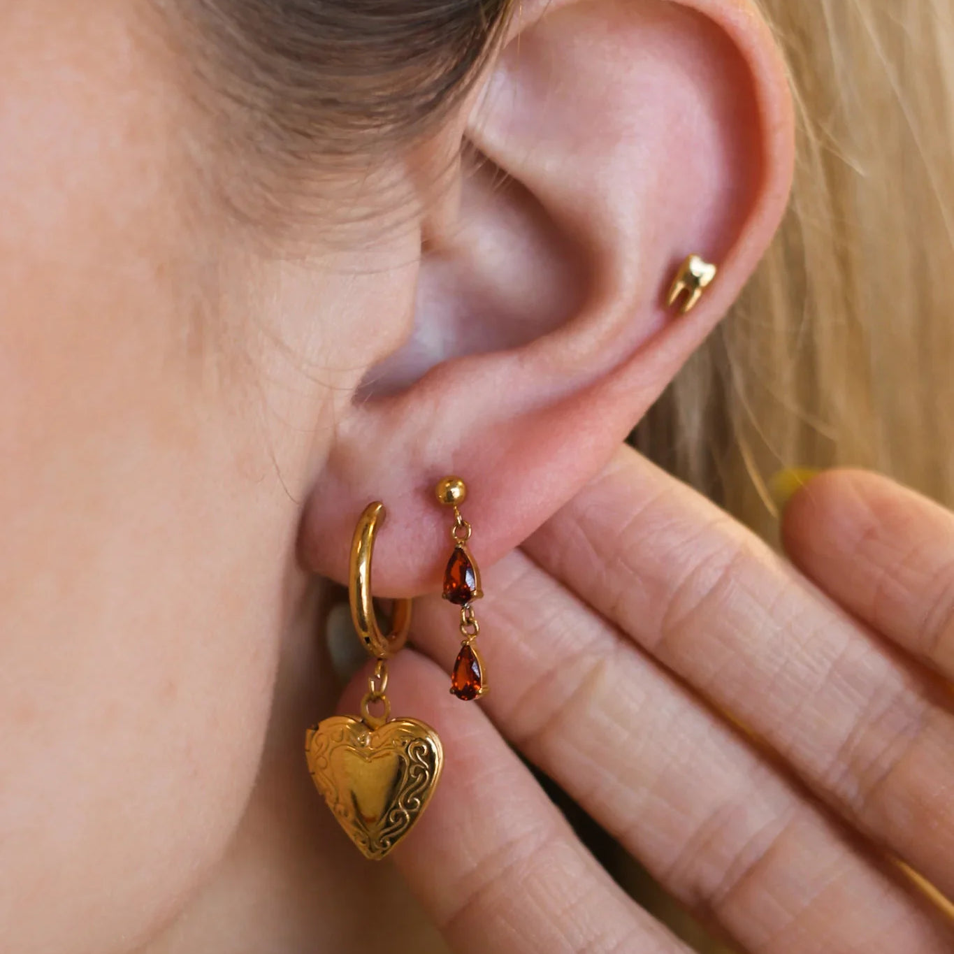 Close-up of a person wearing gold hoop earrings with heart-shaped charms.
