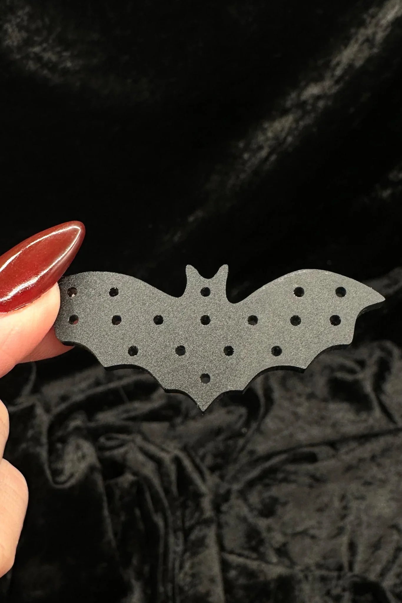 Black lace fabric background with a black bat-shaped acrylic earring organizer held by a hand.