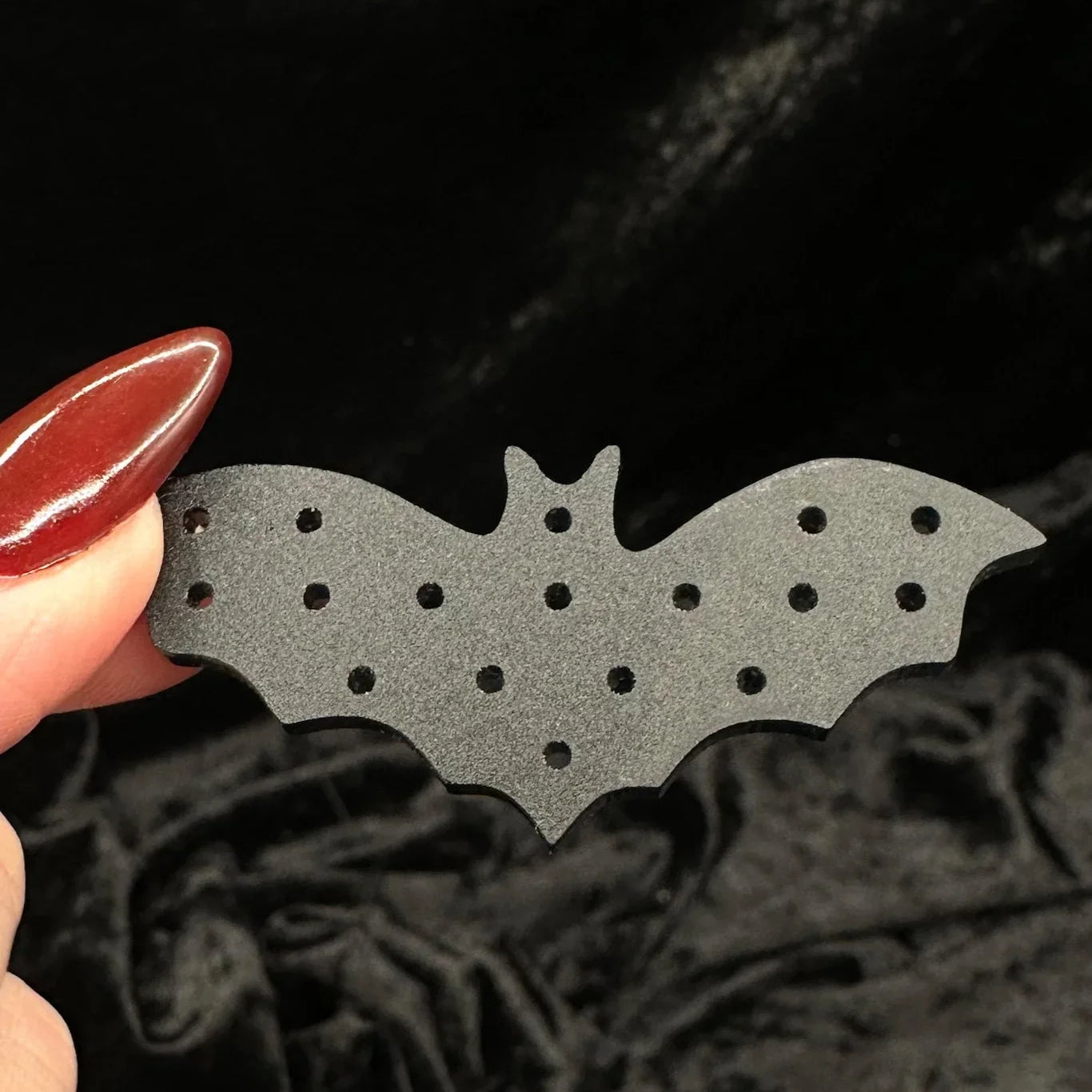 Black lace fabric background with a black bat-shaped acrylic earring organizer held by a hand.