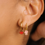 Close-up of an ear wearing gold hoop earrings with red and pink heart charms.