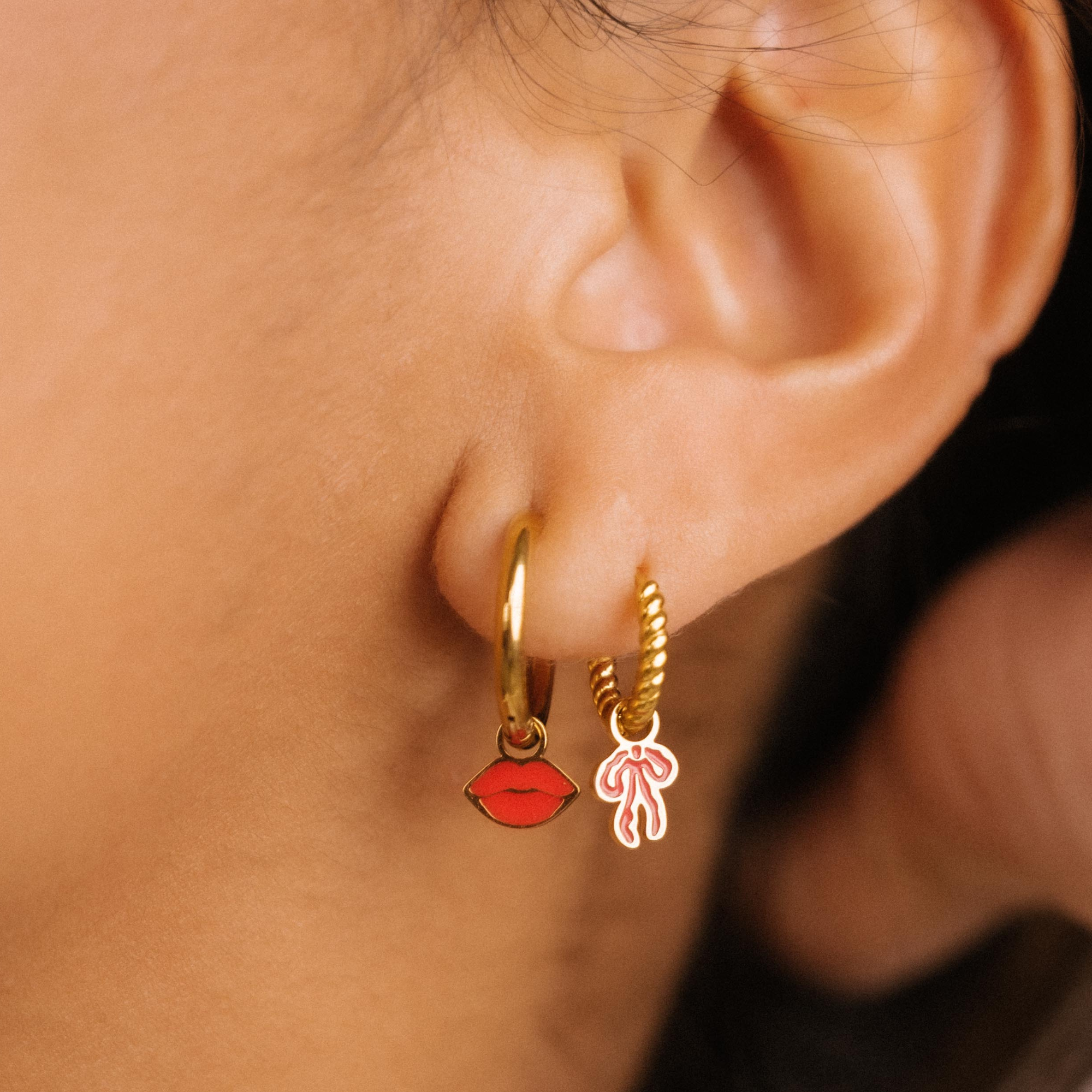 Close-up of an ear wearing gold hoop earrings with red and pink heart charms.