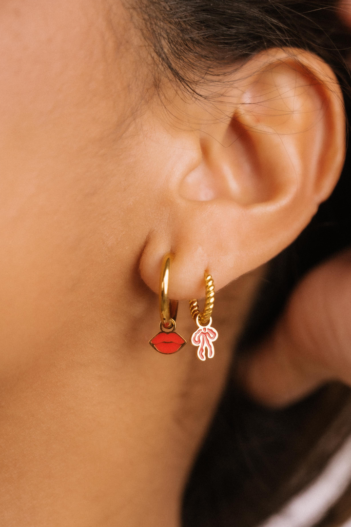 Close-up of an ear wearing gold hoop earrings with red and pink heart charms.