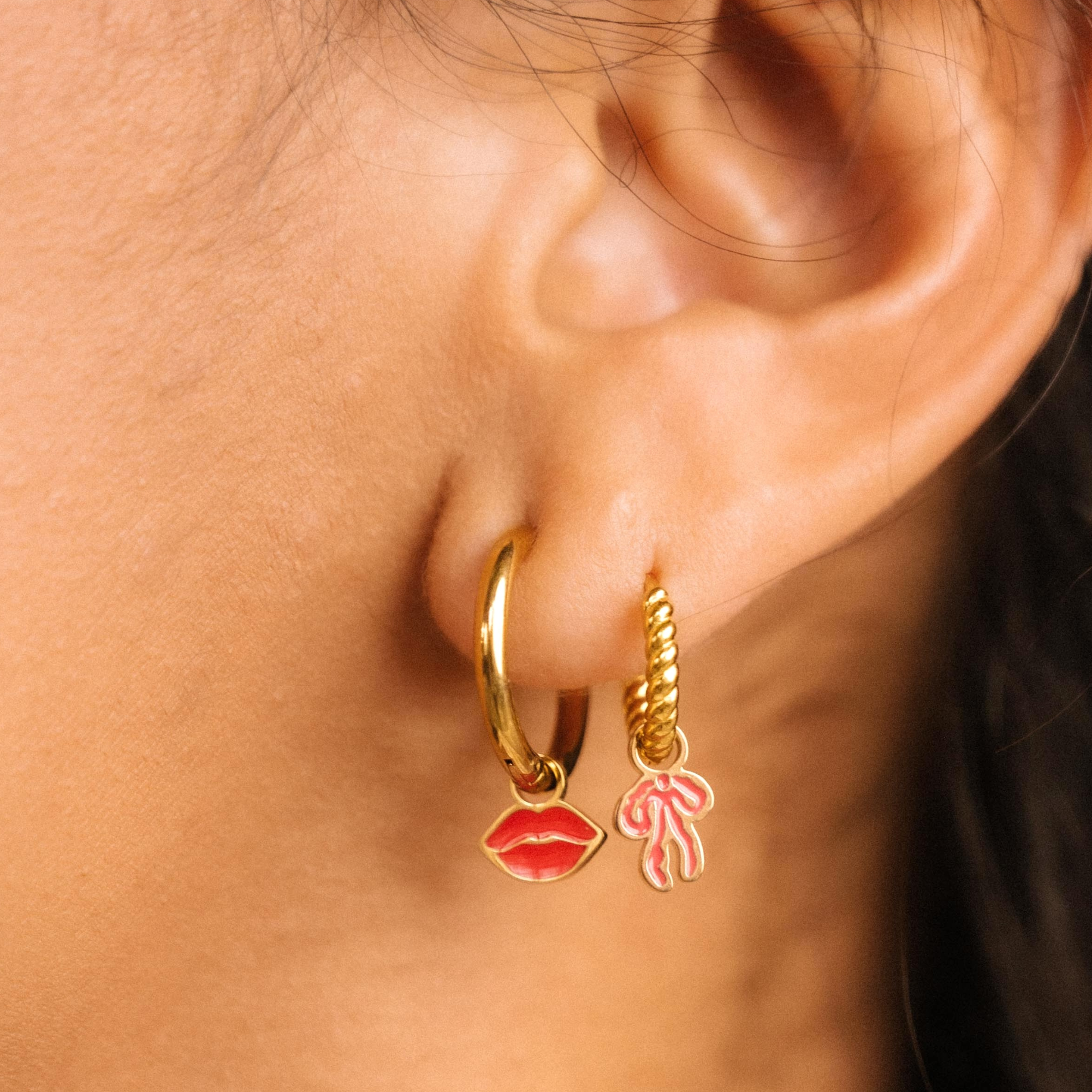 Close-up of an ear wearing gold hoop earrings with lip and flower charms.